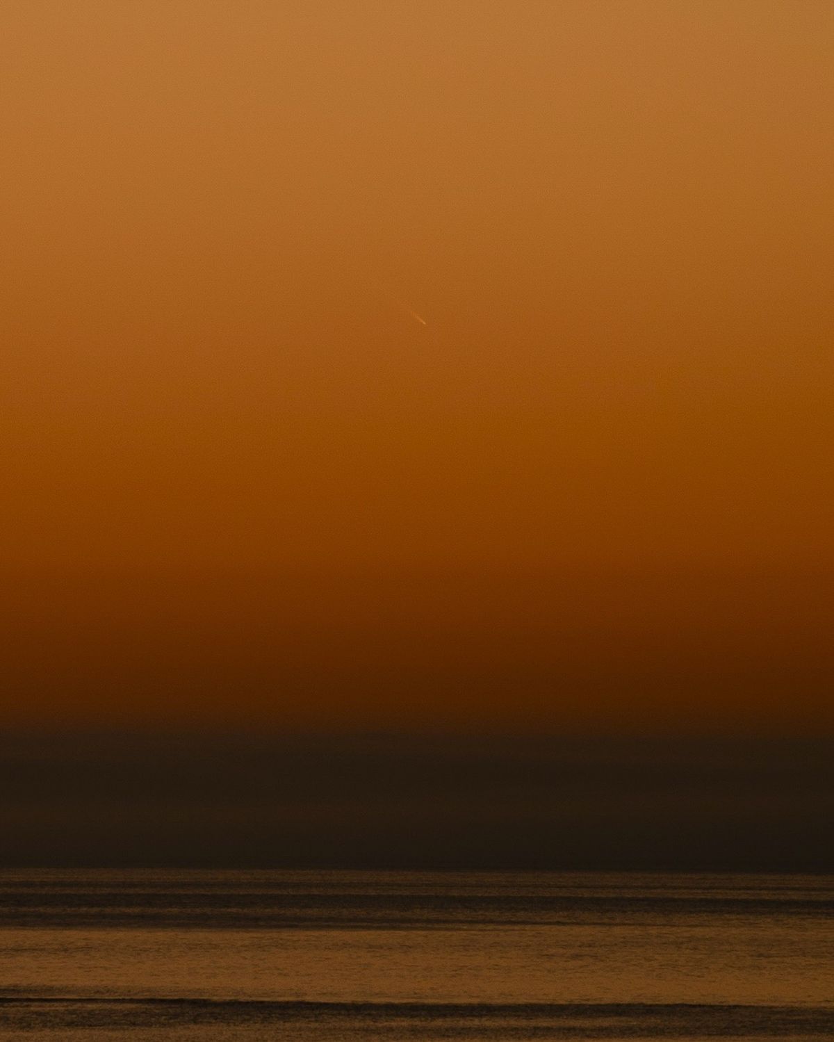 comet above water shining against a deep orange sky.
