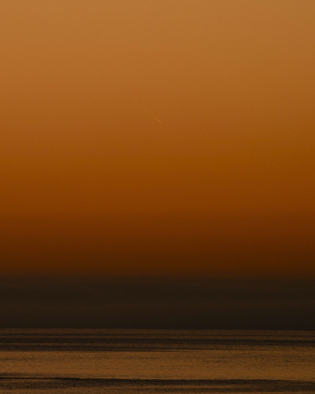 comet above water shining against a deep orange sky.