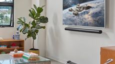 Sonos Arc Ultra underneath TV displaying space scene, in white living room with plant, glass coffee table, wooden bookshelf, and partially open window.