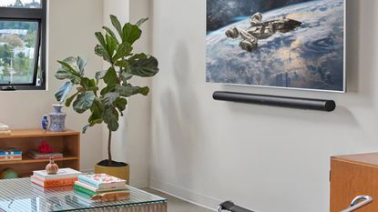 Sonos Arc Ultra underneath TV displaying space scene, in white living room with plant, glass coffee table, wooden bookshelf, and partially open window.