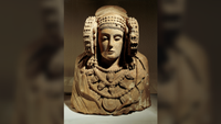 a limestone bust of a woman wearing a cloak, jewelry and large circular ear ornaments