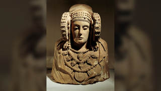 a limestone bust of a woman wearing a cloak, jewelry and large circular ear ornaments