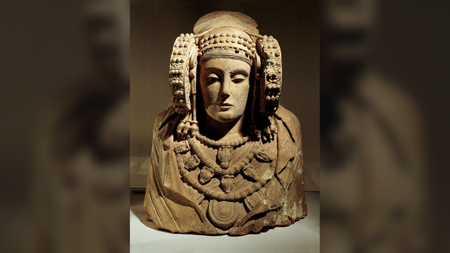 a limestone bust of a woman wearing a cloak, jewelry and large circular ear ornaments