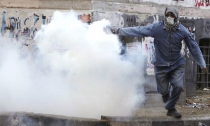 A protester throws a tear gas bomb at riot police