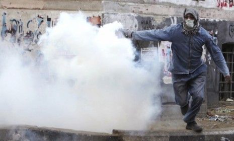 A protester throws a tear gas bomb at riot police