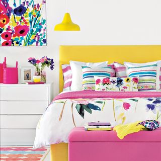bedroom with white wall yellow bed with colourful cushion and painting frame