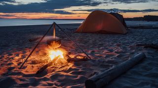A campfire and tent at the beach