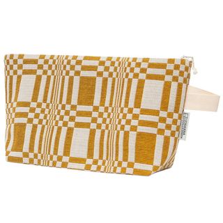 A toiletry bag in ochre and cream stands against a white background that makes its geometrical motifs even more pronounced.