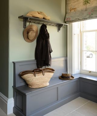 small mudroom near entryway with bench storage seating and peg rail shelf, baskets, coat, stone floor, blind