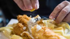 A man squeezes a lemon wedge over a plate of fish and chips, only his hands showing.