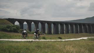 Two cyclists ride alongside Ribblehead Viaduct