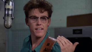 Gary Busey in glasses and standing next to a microphone in The Buddy Holly Story