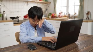 Boy covers his eyes, exhausted from eye strain after long laptop computer use.