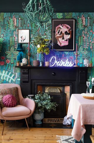 A close-up of a fireplace in the dining room, framed with bold pink and green patterned wallpaper, velvet pink armchair and neon 'Drinks' sign