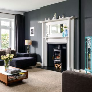 charcoal living room with a mirror above a fire place next to a grey sofa and a wooden coffee table accessorized with flowers