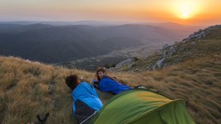 Two campers in sleeping bags on a hillside