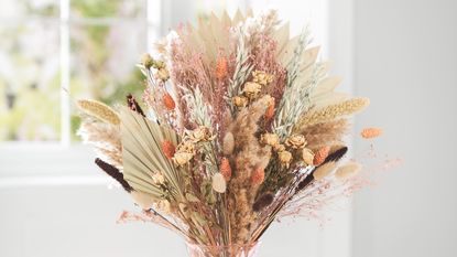 Bunch of dried flowers in glass vase on woven tray