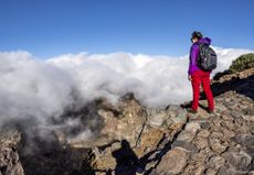 A woman standing on a mountain peak looking at out a rocky landscape.
