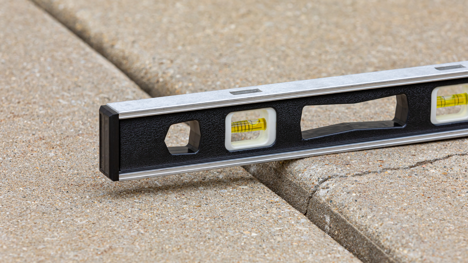 A spirit level resting across two sections of an uneven paved driveway