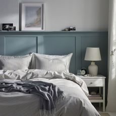 A bedroom with green panelling and a bed dressed in grey and white IKEA bedding