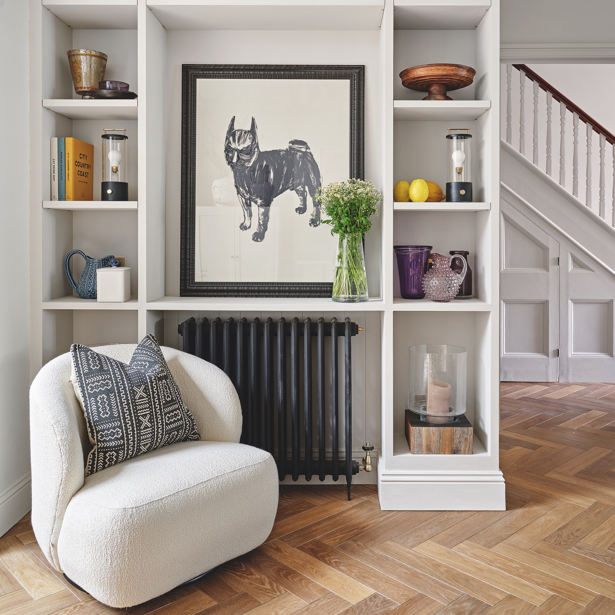 snug area in open-plan kitchen-diner-sitting room, with fitted shelving with accessories and artwork, and white curved armchair