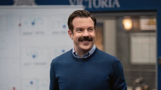 Jason Sudeikis as Ted Lasso in Ted Lasso season 3, standing in front of a white-board.