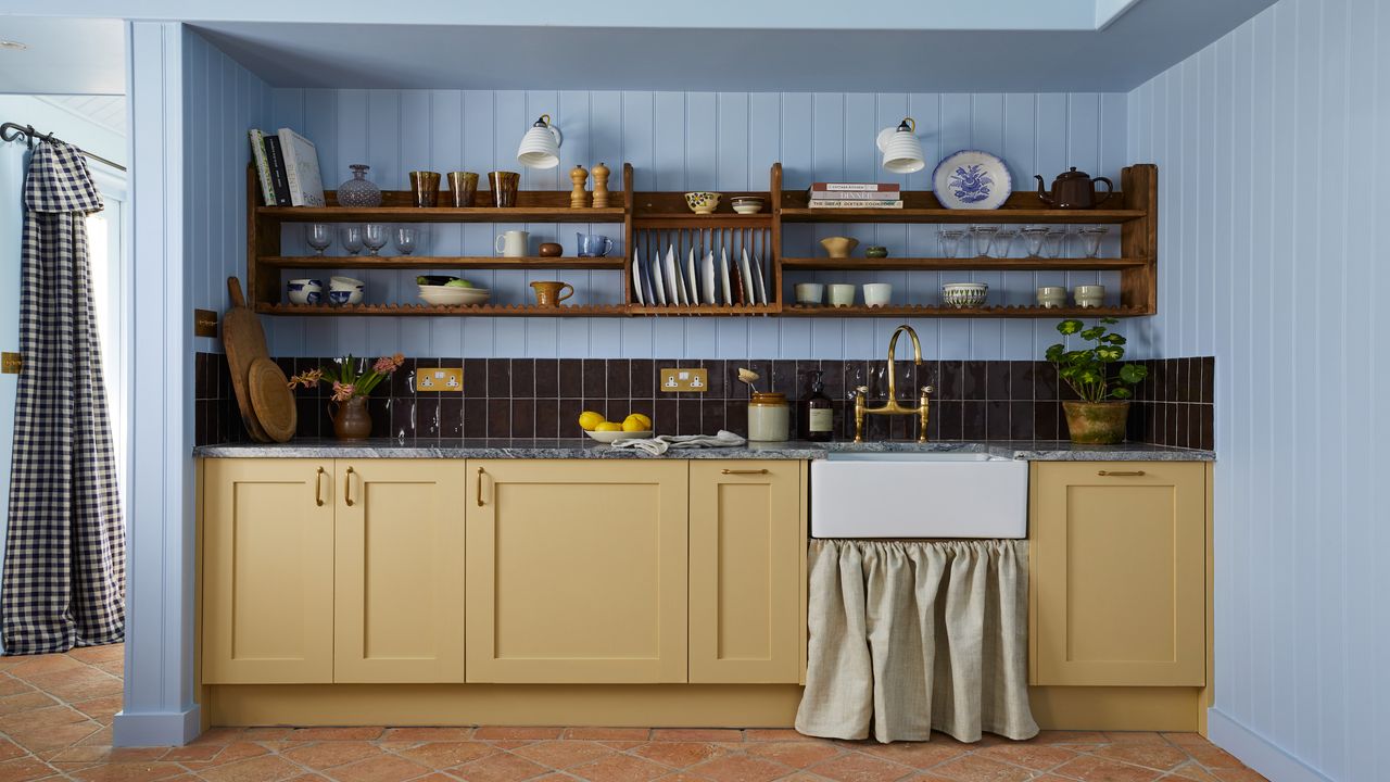 blue kitchen with vertically paneled walls, yellow cabinets, open shelving and a butler&#039;s sink