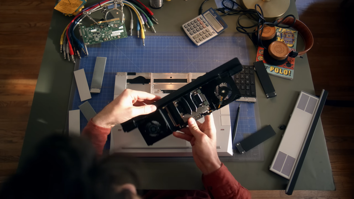 A man holding a component over a partially disassembled Framework laptop.