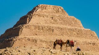 Two camels and a sitting man in front of the Step Pyramid of Zoser, Saqqara, Egypt. We can see 4 steps here.