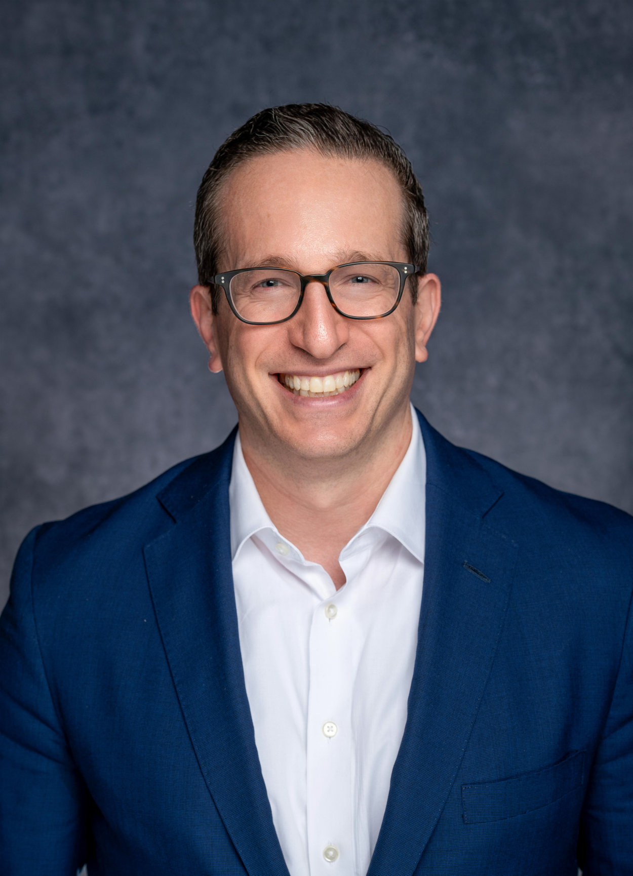 a white man with glasses in a navy blue suit