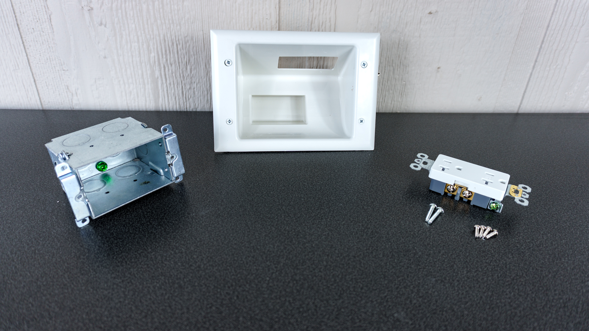 A recessed wall outlet with its plate cover, junction box and receptacle laid out on a table