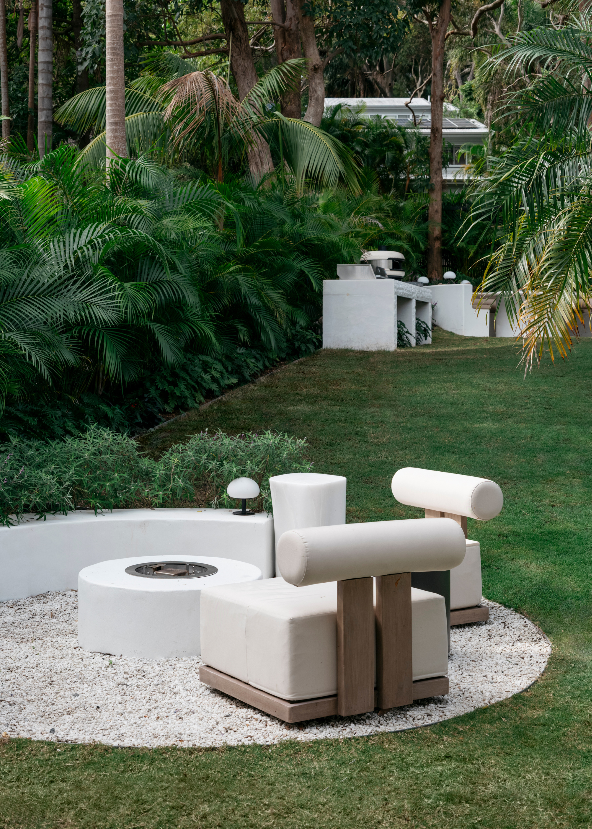 A garden with wood chairs with block off-white cushions around a bench and a circular fireplace