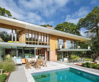 A contemporary new built home with a small pool in front with blue tiles and light coloured paving around