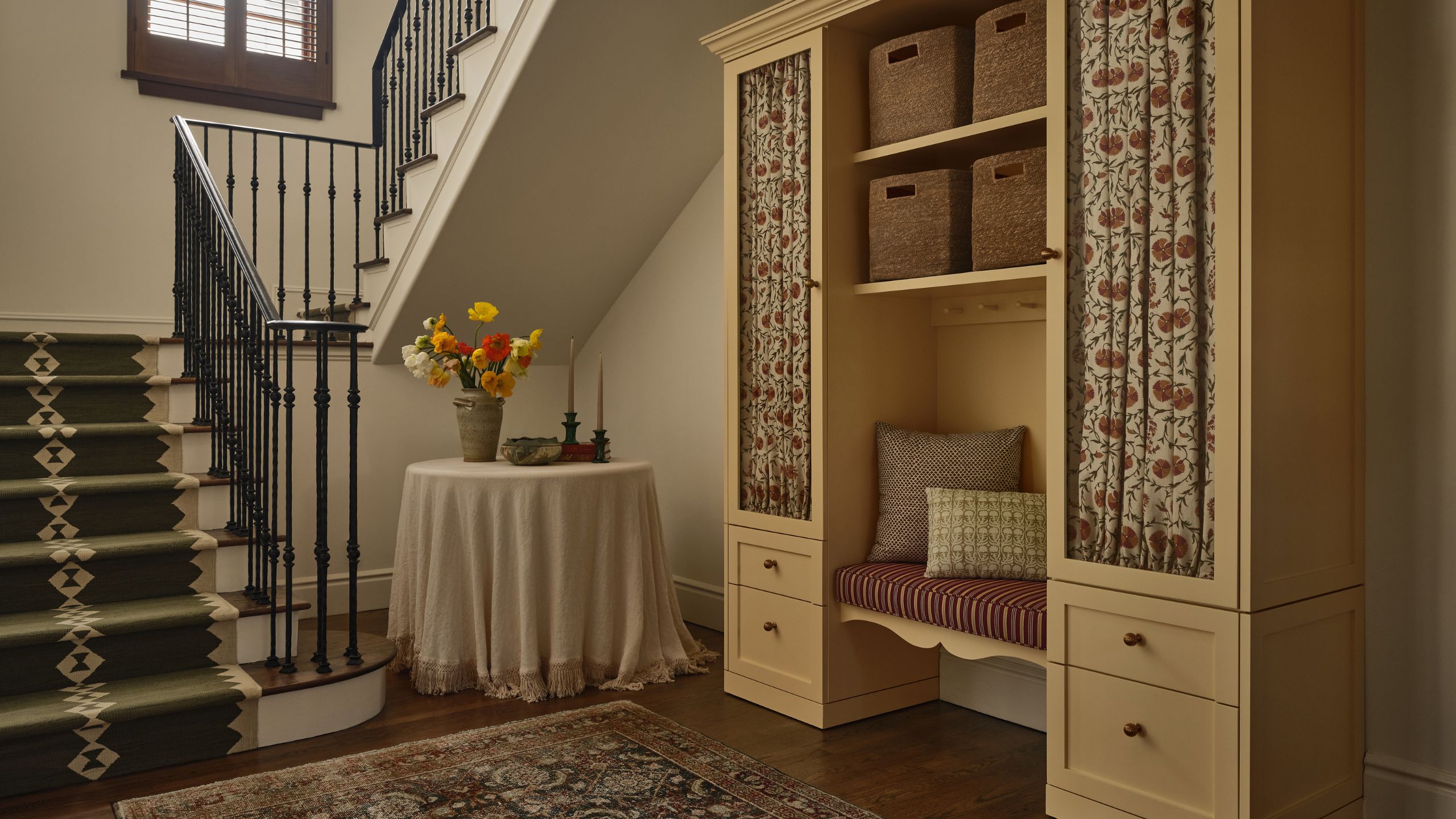 a grand entryway with a yellow painted boot room cabinet with a built-in bench seat and cabinet curtains