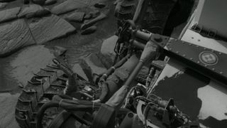 a black-and-white image of a wheeled robot, with deep gouges and cracks in its metal wheels