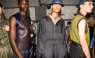 Models wearing hats & dark clothing line up for runway
