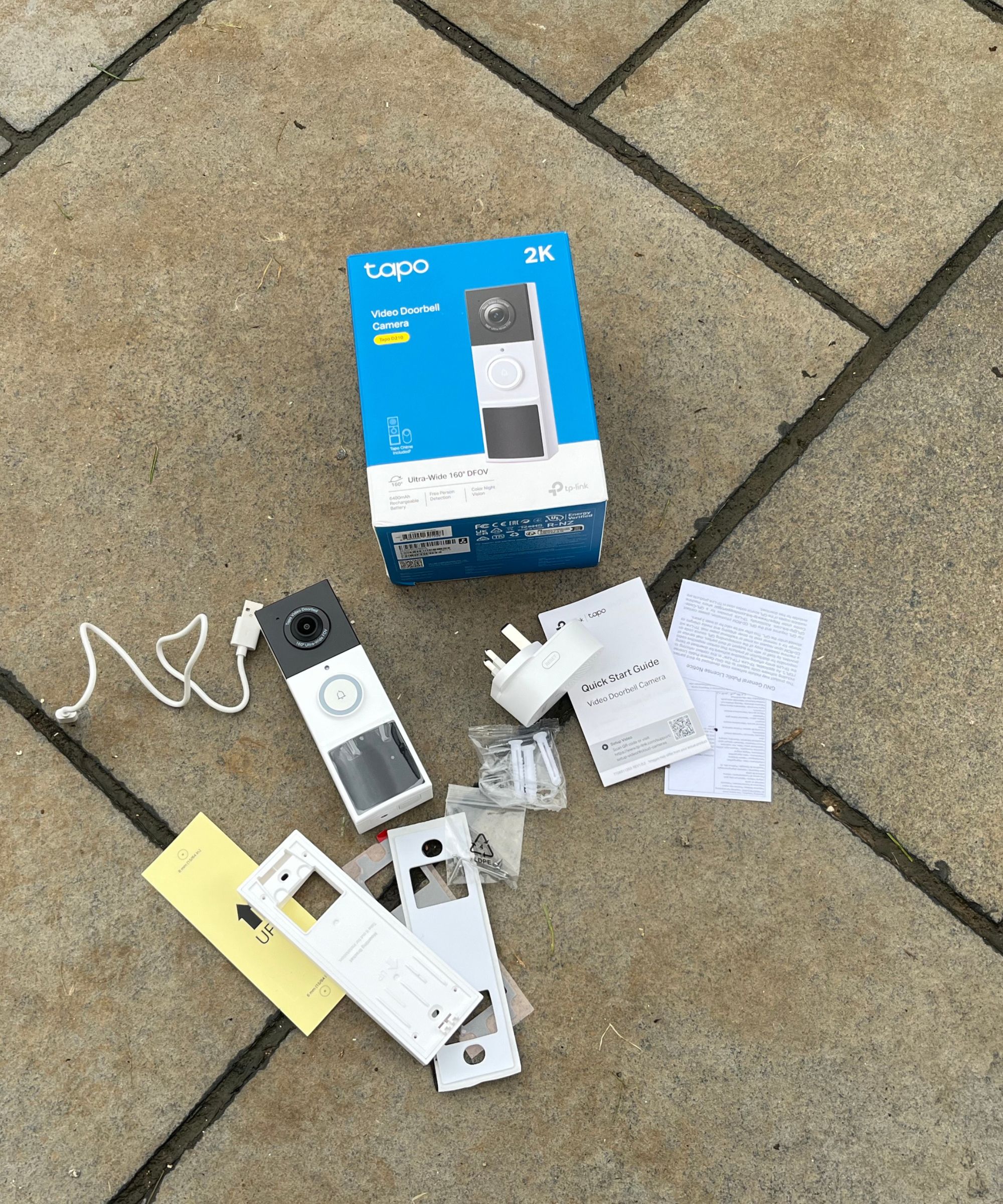 Every part of the Tapo D210 Video Doorbell kit unboxed on tiled concrete floor.