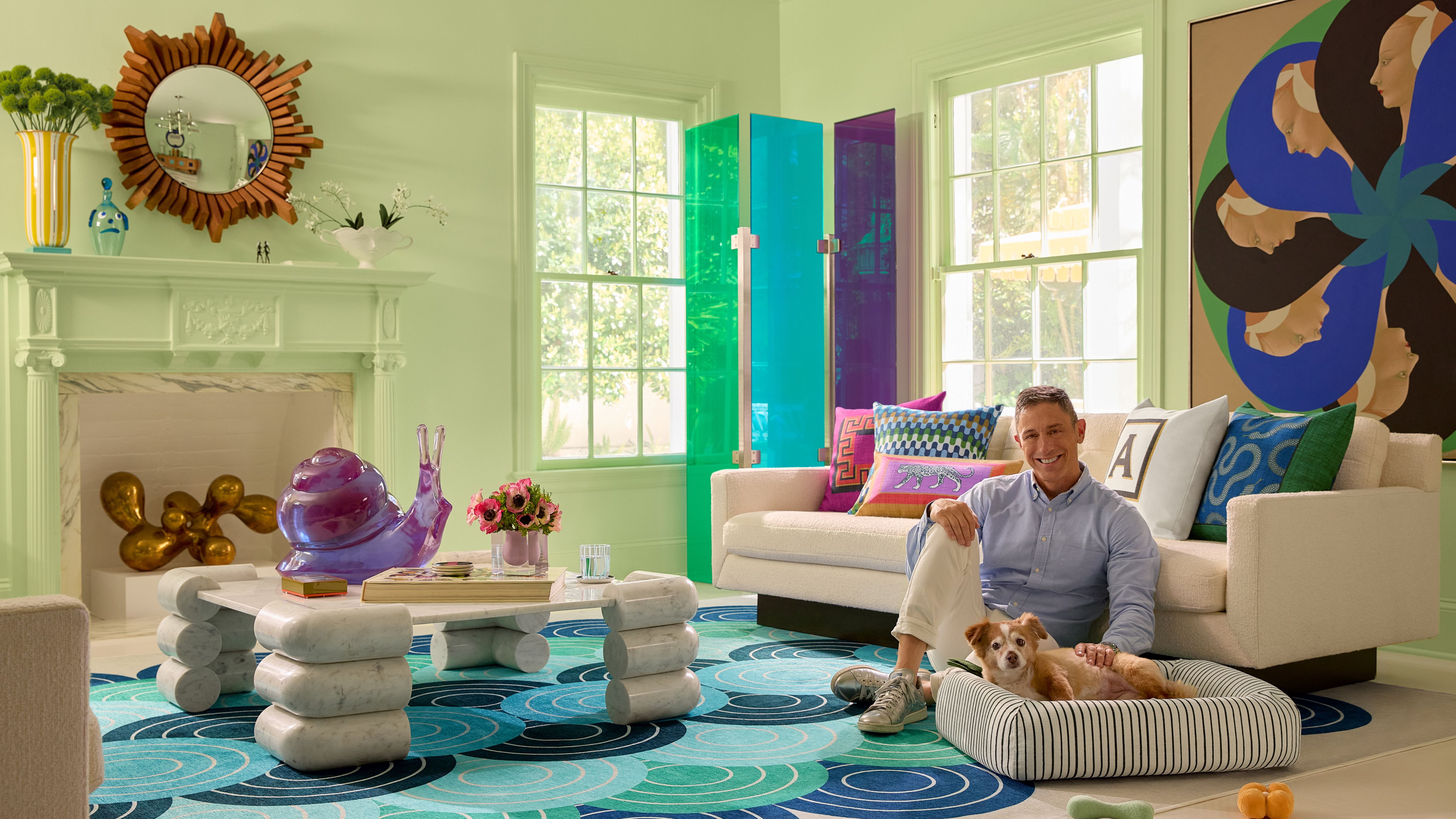 Potter and designer Jonathan Adler posing with his pet daughter, FoxyLady, in a mint-hued living room that is anchored by a blue scallop-patterned rug and geometric pet bed from his new Ruggable home accessories collection