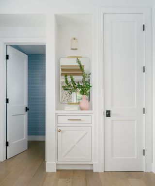 A white entryway with a small nook and a door leading into a room with blue wallpaper
