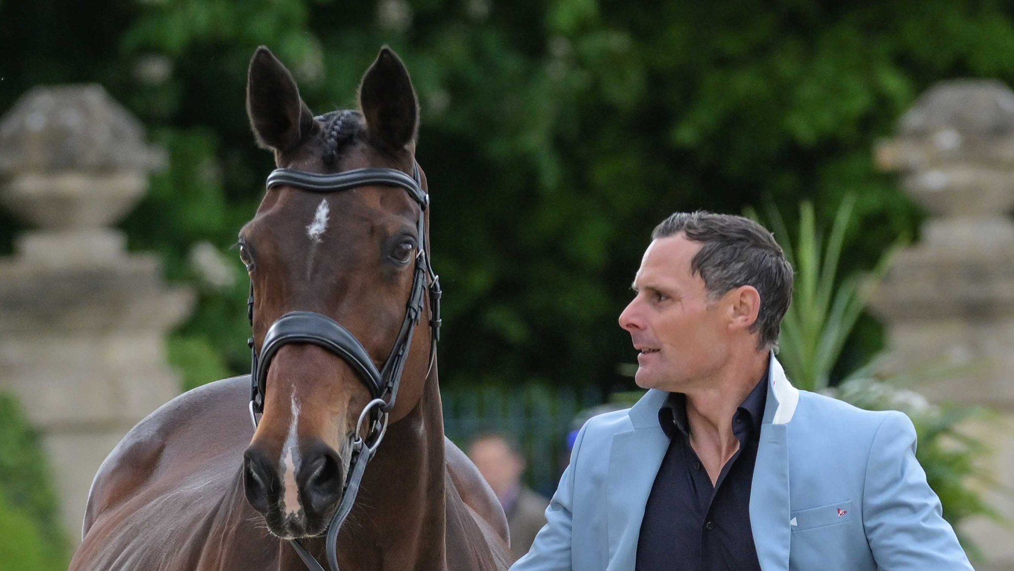 Alex Bragg looks towards his Badminton ride Quindiva, who is a bay mare with pricked ears wearing a snaffle bridle, as he presents her for the first horse inspection at Badminton