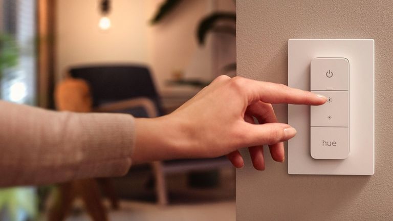 best smart light switch 2022, showing Philips Hue dimmer switch on a wall, being pressed by a woman's hand
