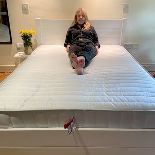 A woman with blonde hair wearing a black denim jumpsuit laid on the Dreams Workshop Follows Traditional Spring Mattress