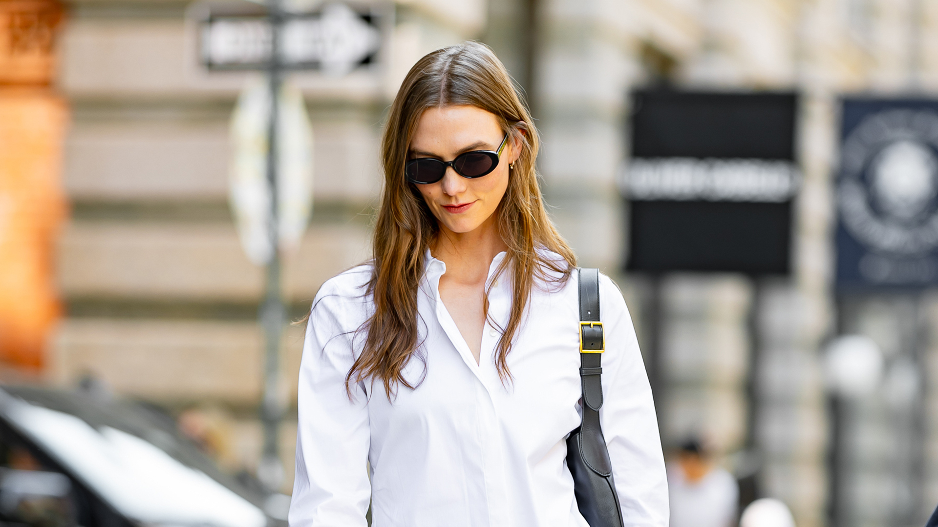 Karlie Kloss wearing a cinched button-down, a black skirt, a black bag, and black open-toe sandals 