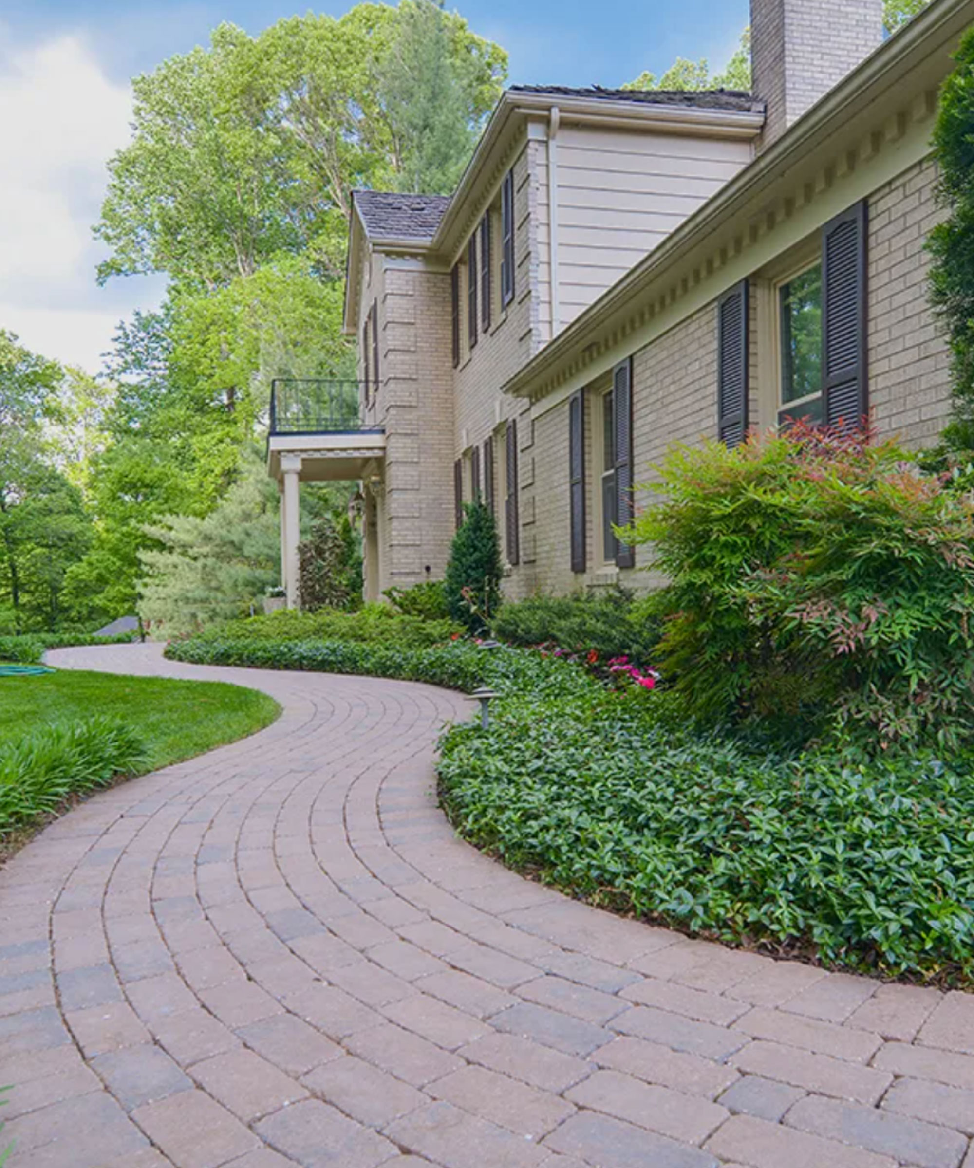 curved brick path leading up to porch in front yard, with flowerbeds on one side of the path and lawn on the other side, plus trees and shrubs