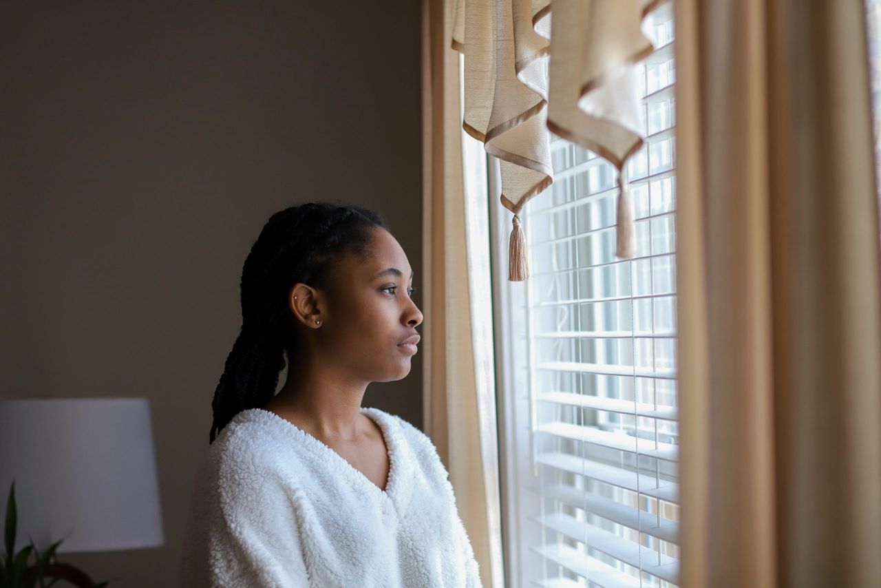 Young woman looking out of window during lockdown after having vivid dreams