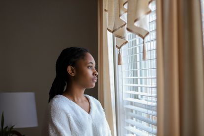 Young woman looking out of window during lockdown after having vivid dreams