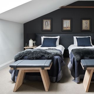Two twin beds with grey, white and blue bedding in front of dark grey feature wall and on top of soft grey carpet