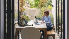 A woman sits outside on her patio looking at her laptop.