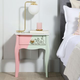 pink and green bedside table next to white bed and lamp