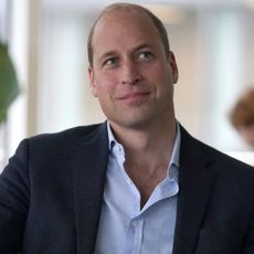 Prince William wears a navy suit and a light blue shirt and smiles awkwardly